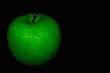 Green ripe apple with water droplets on a dark background, closeup