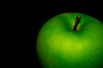 Green ripe apple with water droplets on a dark background, closeup