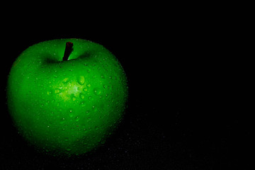 Green ripe apple with water droplets on a dark background, closeup