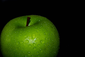Green ripe apple with water droplets on a dark background, closeup