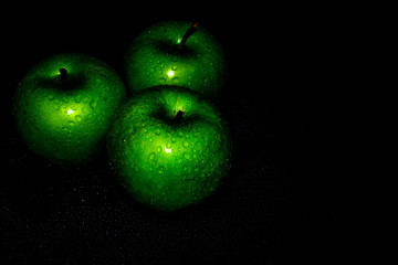 Green ripe apple with water droplets on a dark background, closeup