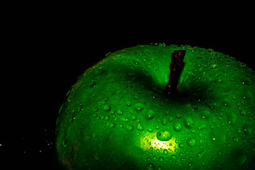 Green ripe apple with water droplets on a dark background, closeup