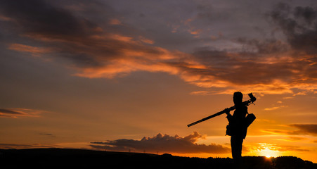 Silhouette of photographer with tripod against setting sun