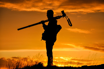 Silhouette of photographer with tripod against setting sun
