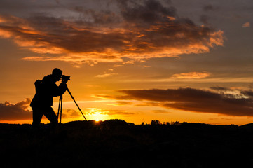 Silhouette of photographer with tripod against setting sun