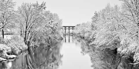 Snow capped trees reflecting on a river with viaduct in the background