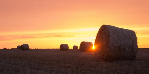 Sun shining between hay bales with orange sky