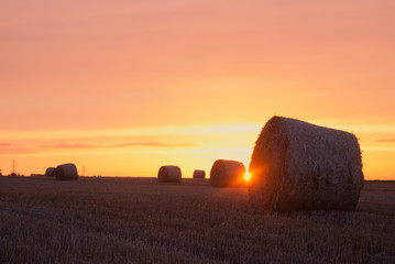 Sun shining between hay bales with orange sky