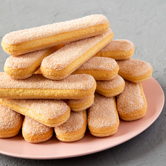 Savoiardi or ladyfingers cookies on a pink plate over gray background, side view. Close-up.