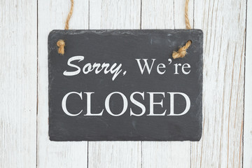 Sorry we're Closed text on a hanging chalkboard on weathered whitewash textured wood
