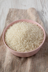 Dry white rice basmati in a pink bowl over white wooden background, side view. Close-up.