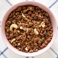 Homemade chocolate granola with nuts in a pink bowl, overhead view. From above, top view, flat lay.