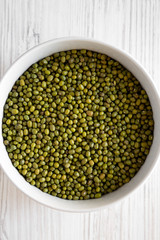 Raw green mung beans in a gray bowl over white wooden surface. Flat lay, top view, from above. Close-up.