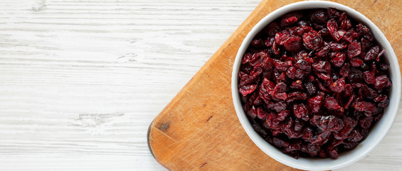 Dry organic cranberries in a gray bowl on rustic board over white wooden surface, top view. Overhead, from above, flat lay. Copy space.