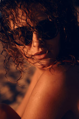 Toned woman in sunglasses and curly hair resting in the summer on the beach in the evening