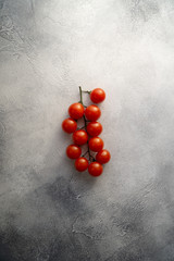 Bunch of cherry tomatoes on white stone concrete table, top view with copy space. Ingredients for cooking.