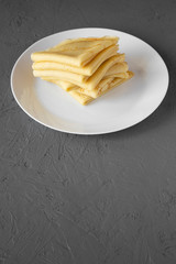 Pile of tasty blini on a white plate over gray background, side view. Copy space.
