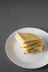 Pile of tasty blini on a white plate over gray surface, side view. Copy space.