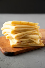 Pile of tasty blini on a rustic wooden board over concrete background, side view. Close-up.