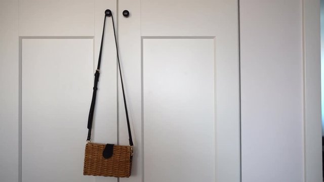 Sliding shot of a delicate and small wicker bag hanging from a wardrobe, on a white and minimal room