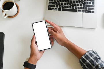 Cropped shot top view of businessman hands using smartphone mockup on office desk. Blank screen mobile phone for graphic display montage.