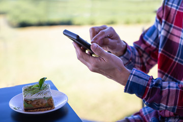 Happy time of young man using smart phone taking photo which take a picture food or  green tea cake of bakery before eating, photography on in the coffee shop