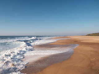 Empty long wide beach, yellow sand, Nazare; big portugal curling wave; power energy of nature; beautiful atlantic ocean background; wave for surfing camp; sport leisure activity; splashing wave crest