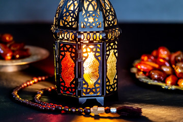 The Muslim feast of the holy month of Ramadan Kareem with dates on a tray on a dark background. Beautiful background with a shining lantern Fanus. © Ievgenii Meyer