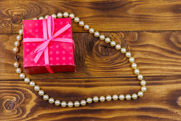 Gift box and pearl necklace on wooden background