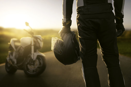 Motorradfahrer steht vor seinem Motorrad im Sonnenuntergang