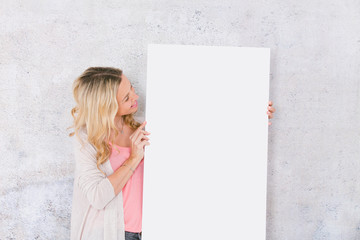 beautiful blond woman is holding white card for copy space in front of grey background