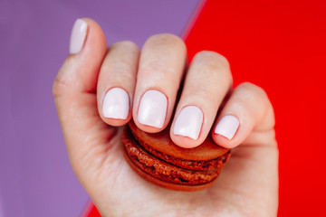 Hand with light rose manicure with colorful macarons. Isolated at bright background.