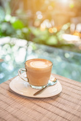 Hot coffee on the glass table over blurred garden background with vintage morning warm light