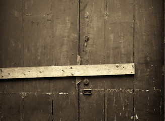 sepia close up of an old cracked peeling wooden plank door barred shut with a piece of timber and...