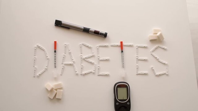 Composition with the word DIABETES is from the Lancet, insulin syringe and sugar cubes, lying next to a blood glucose meter and an insulin syringe pen.