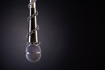 Microphone with a chain, depicting the idea of freedom of the press or freedom of expression on dark background. World press freedom day concept.