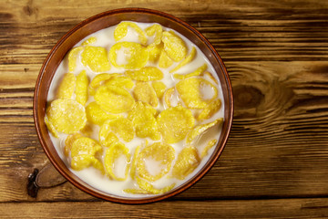 Cornflakes with milk in a bowl on wooden table. Top view