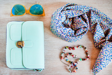 Fashion handbag with glasses, scarf, beads on gray wooden table. Background.