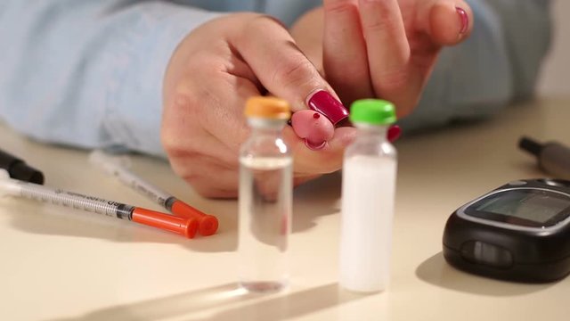Close-up of a girl with type 1 diabetes measures blood glucose with a glucometer, she squeezes a drop of blood from her finger. In front of a bottle of insulin, syringe and glucometer. Insulin therapy