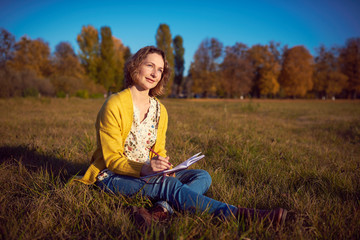 Fototapeta premium Woman with a notebook on the grass in the park in autumn