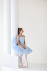Obraz na płótnie Canvas A cute ballerina in ballet costume and in pointe is dancing in a white studio. Girl in the dance class. The girl is studying ballet. Ballerina is dancing. Beautiful dancer practicing by the mirror.