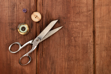 Vintage scissors and buttons, shot from the top on a dark rustic wooden background with a place for text
