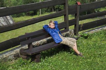 White boy sitting on wooden bench at countryside landscape background. Horizontal color photography.