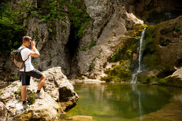 Young man on trekking take photo of a waterfall in forest