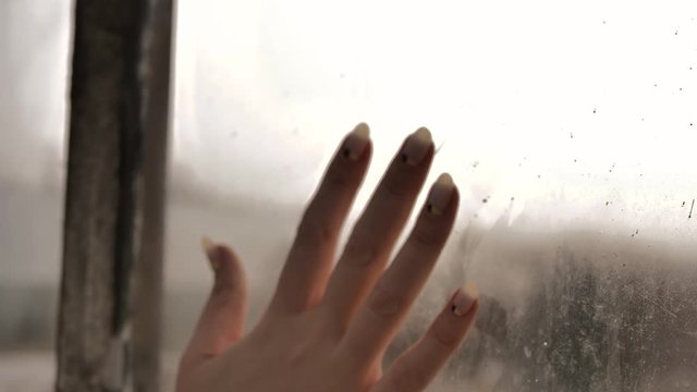 a woman's hand slides over a misted window, leaving streaks on the glass
