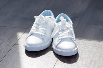 White leather female sneakers shoes on laces on grey brown wooden background. Shy girl content.
