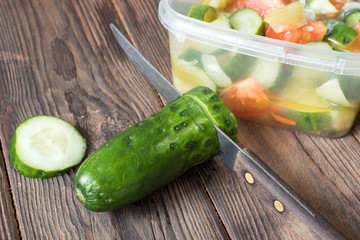 knife and cucumber lie next to a plate of salad, healthy food concept, vegetarianism.