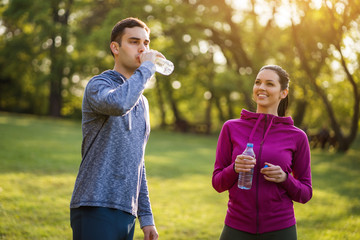 Obraz premium Young couple exercising in park. They are drinking water. 