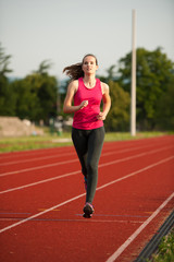Obraz premium Beautiful young woman runner run on a track in early summer afternoon
