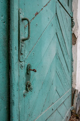An old wooden door painted with cracked green paint. Rusty key in the keyhole.